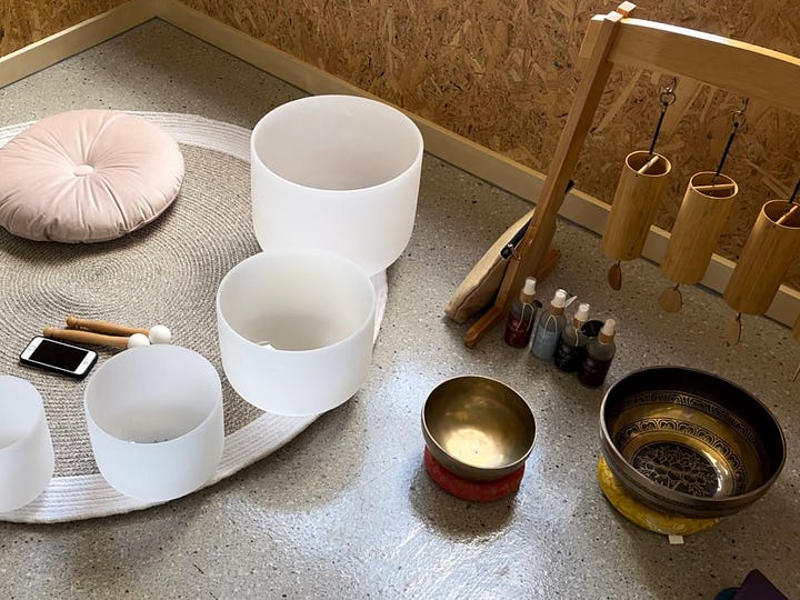 Photo 1: crystal singing bowls sitting on a mat with a set of chimes and metal singing bowls off to the side. Photo 2: three people sitting at a table and writing.