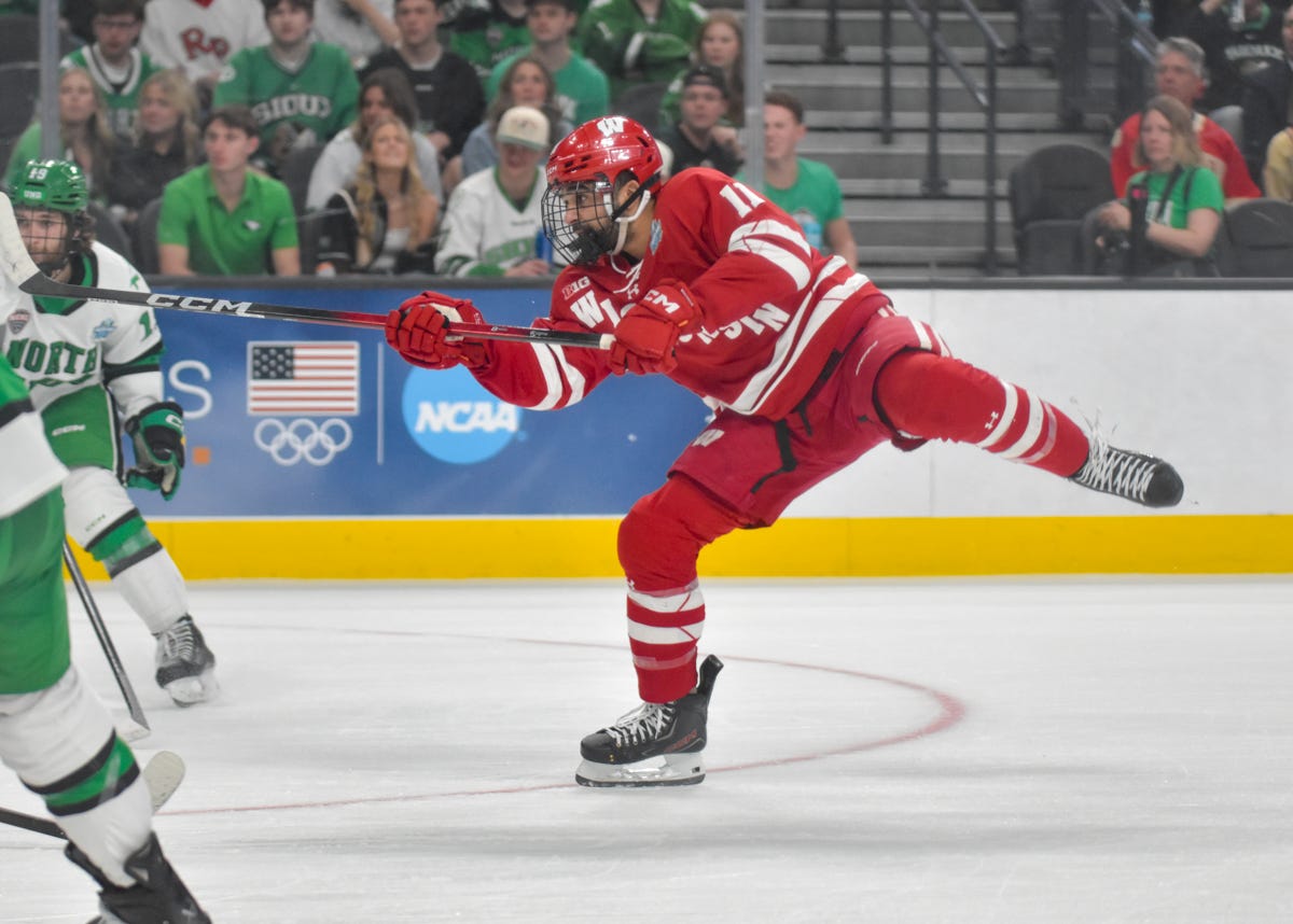 wisconsin hockey forward Simon Tassy Shoots the puck while lifting his left foot in the air