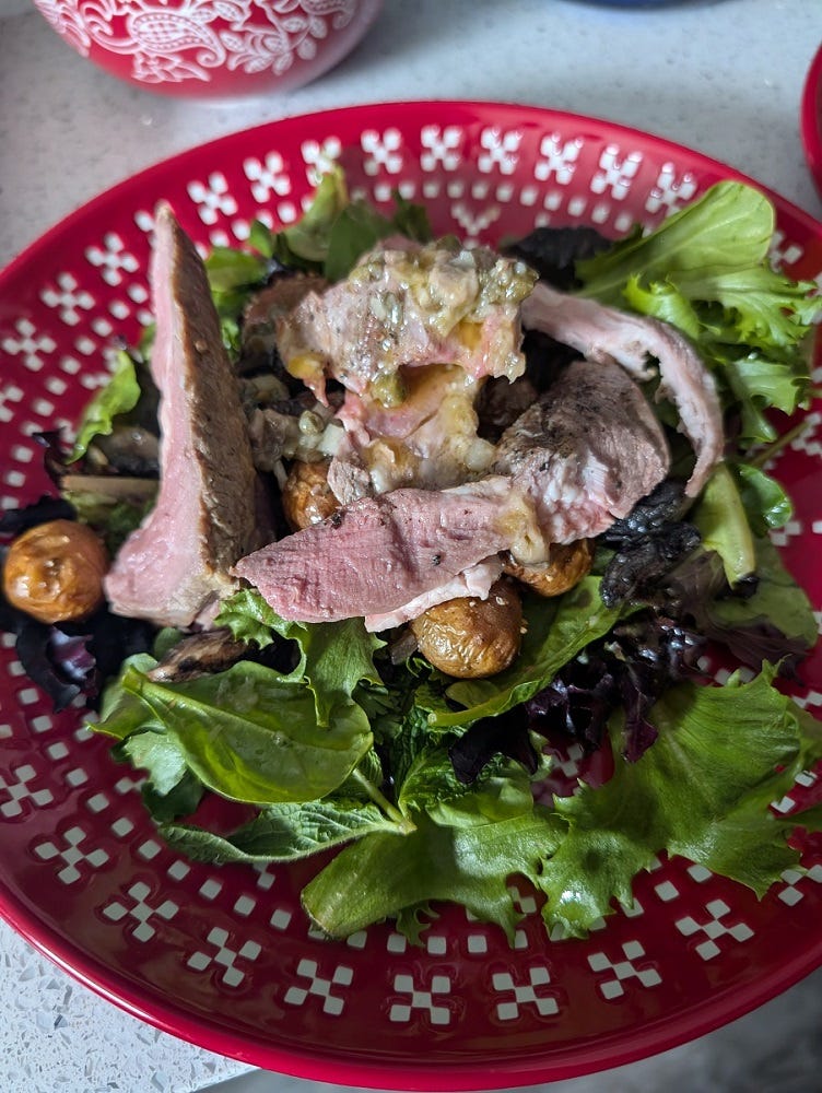 A salad of greens, meat, and potatoes on a red plate