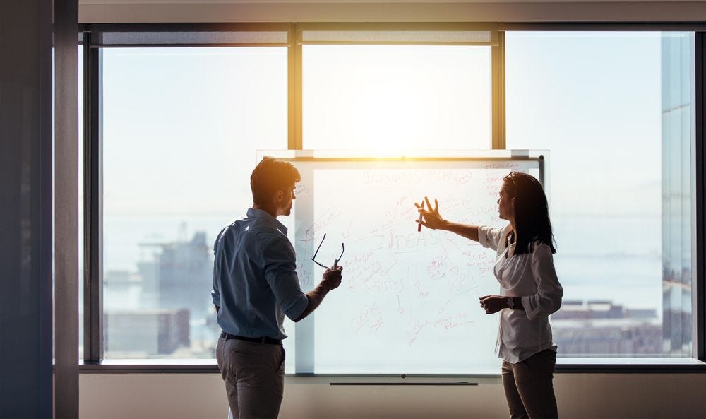 Young creatives drawing on whiteboard in bright conference room