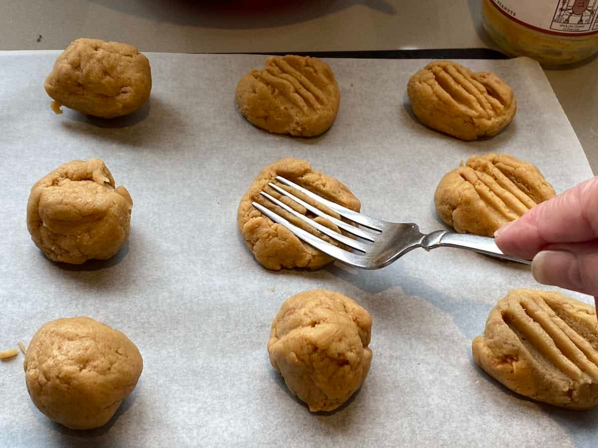 Unbaked Peanut Butter cookie dough on a baking tray, being flattened by a fork. Unbaked Peanut Butter cookie dough on a baking tray, being flattened by a fork.