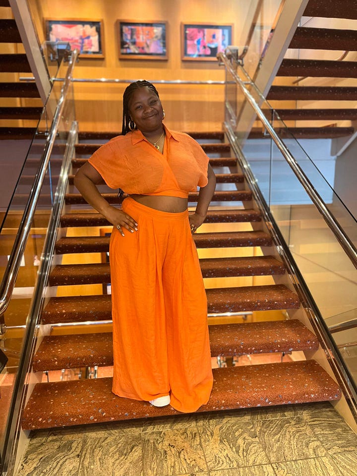 Left to right: Black women similing in the hallway near an elevator dressed in a blue silk outfit. Black women standing a hallway near an elevator on a cruise ship dressed in a brown matching outfit. Black woman admires the sea at night on a cruise ship dressed in a green sheet matching pants set. Black woman poses on a stair case in orange matching set.