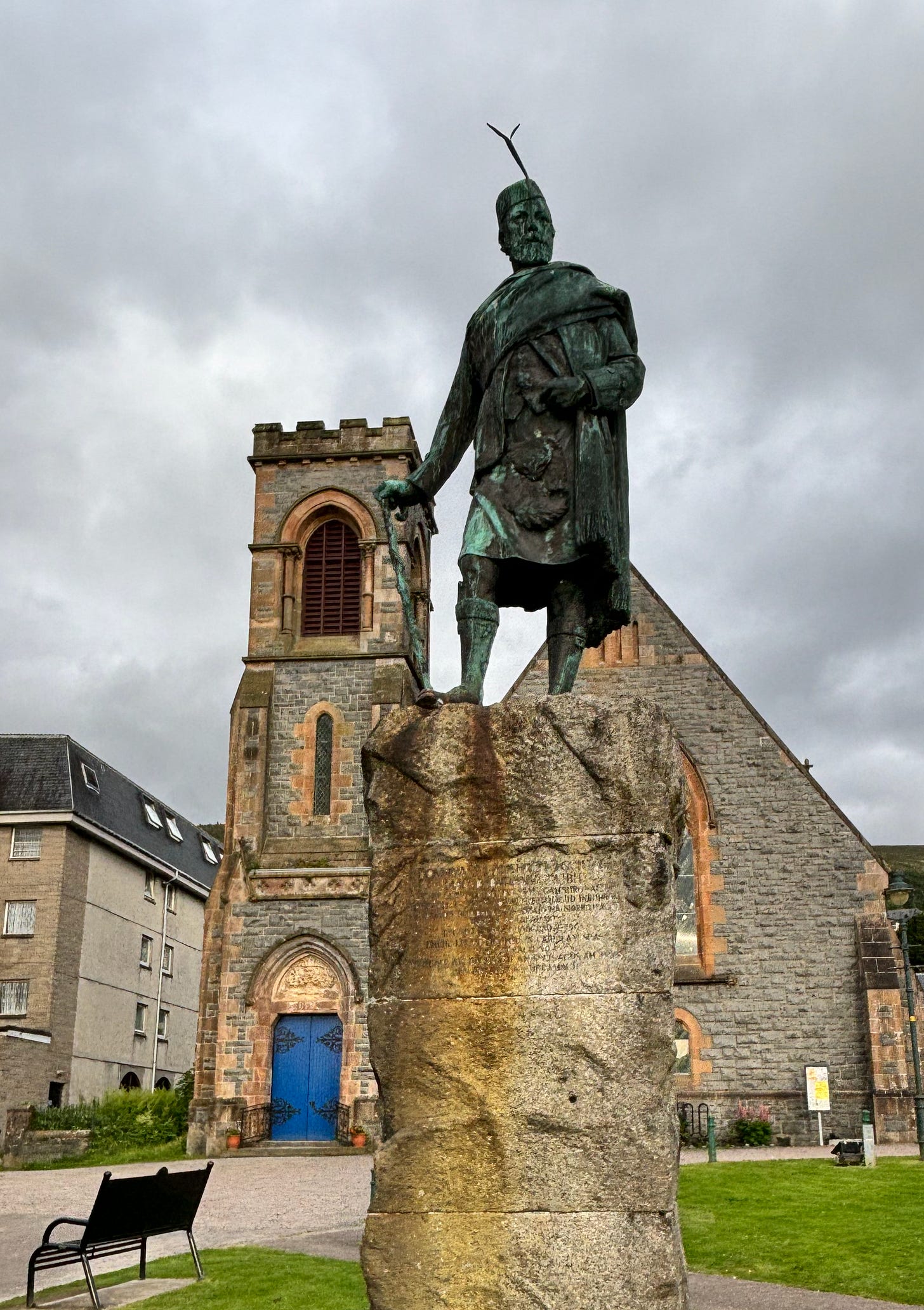 Oxidized bronze statue in Fort William, Scotland outside Church of Scotland with blue door.