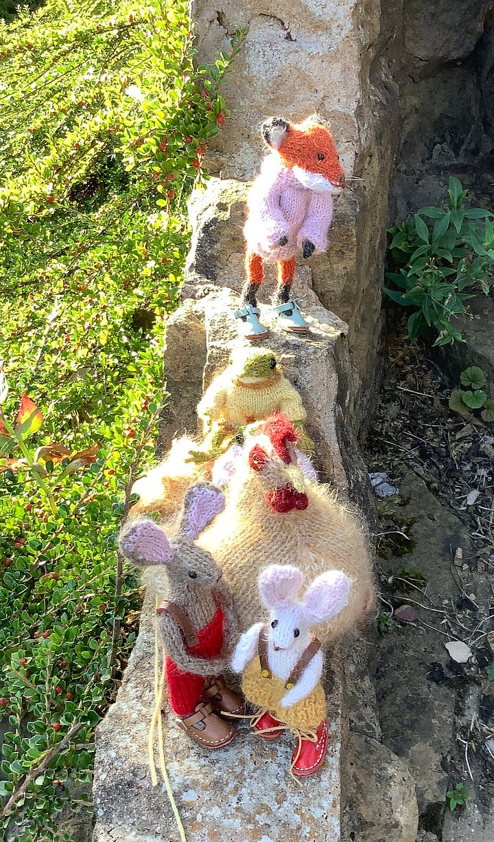 Knitted toys atop a stone wall with foliage in the backgroud