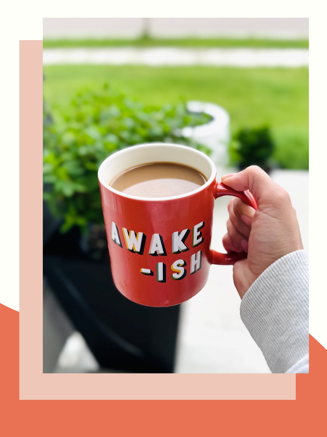 salmon pink mug with the text "awake-ish" held in front of an outdoor landscape