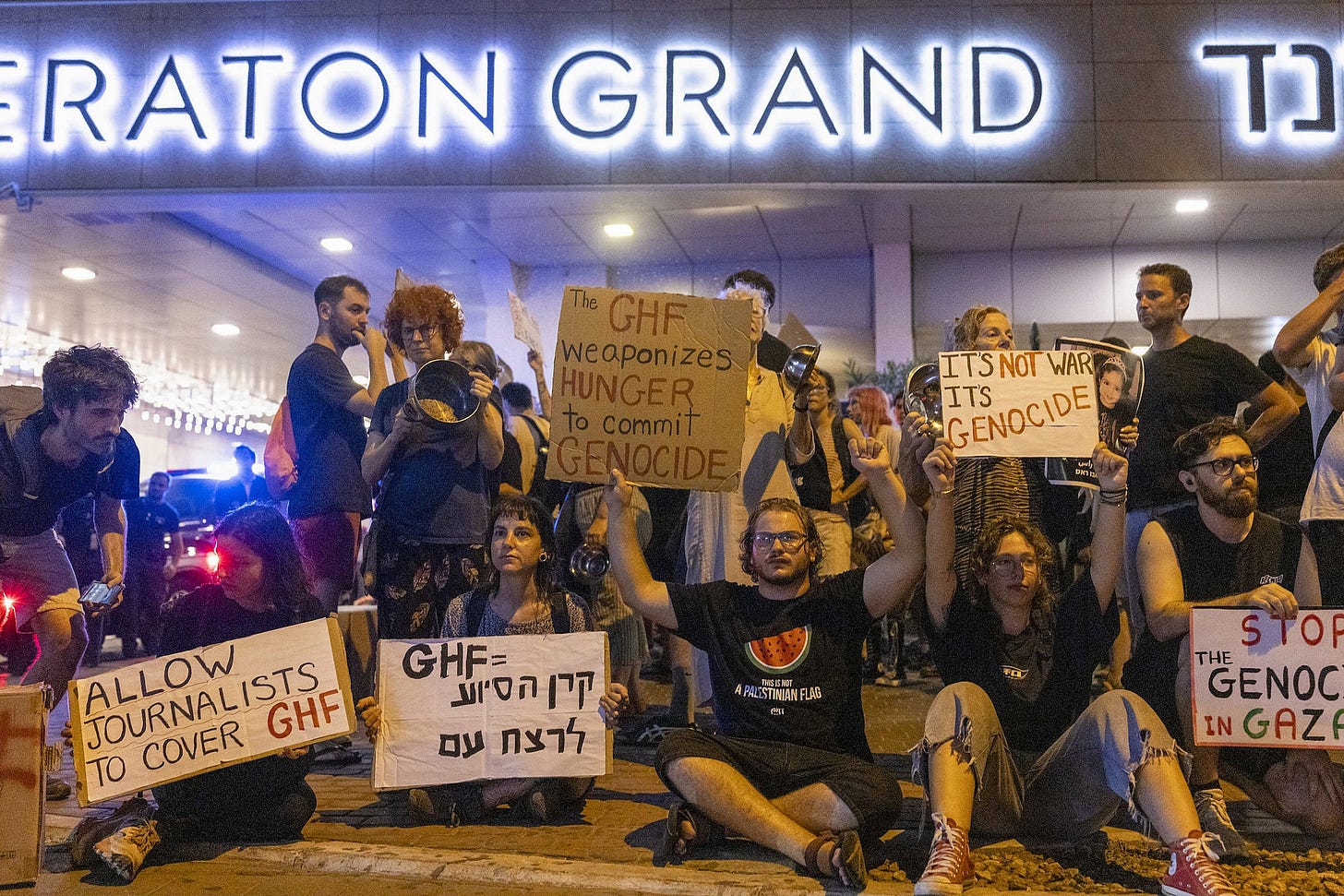 I manifestanti a Tel Aviv tengono cartelli che denunciano la Gaza Humanitarian Foundation (GHF) per il suo ruolo nel genocidio e nella fame a Gaza, il 13 agosto 2025. (Oren Ziv/Attivestills) I manifestanti a Tel Aviv tengono cartelli che denunciano la Gaza Humanitarian Foundation (GHF) per il suo ruolo nel genocidio e nella fame a Gaza, il 13 agosto 2025. (Oren Ziv/Attivestills)