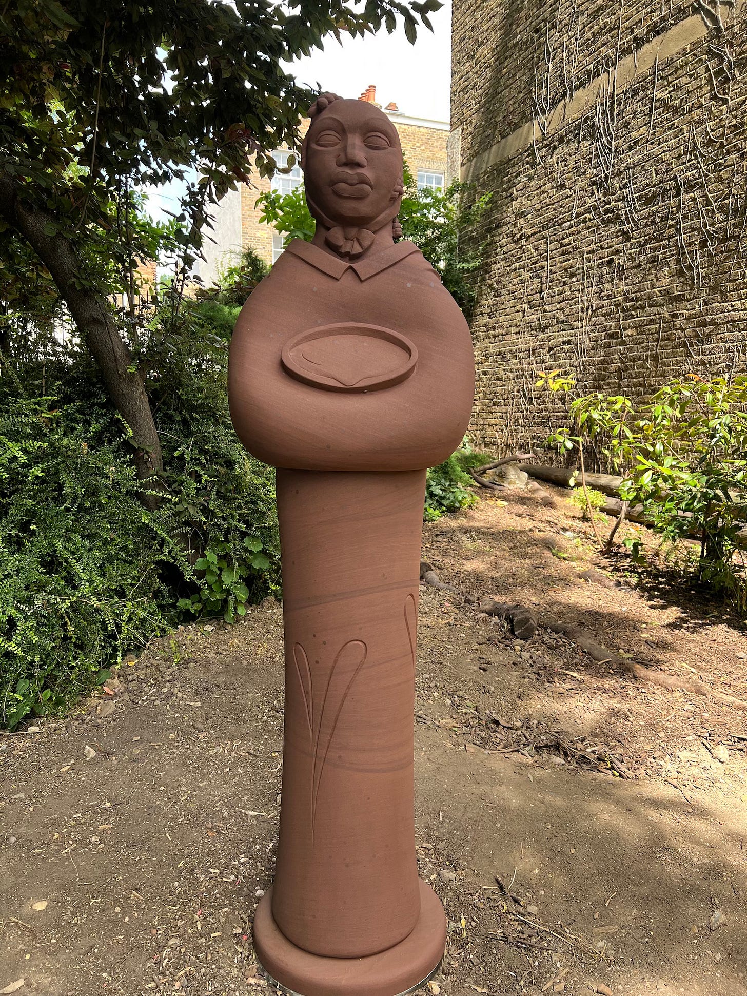 Life size statue of Mary Wollaston holding a bowl of water, in red sand stone