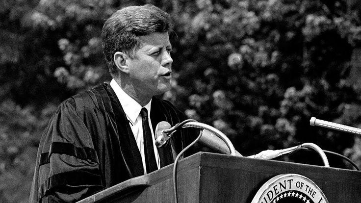 This may contain: a man standing at a podium in front of a microphone and wearing a graduation robe