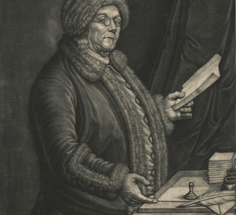 Black and white mezzotint on paper of man in spectacles and fur hat holding a book in his left hand. His right hand gestures to a quill and piece of paper on the desk in front of him