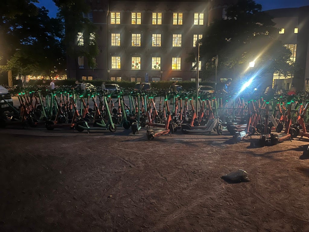 Rows of orange electric scooters on a street at night. Handlebars are lit up in green