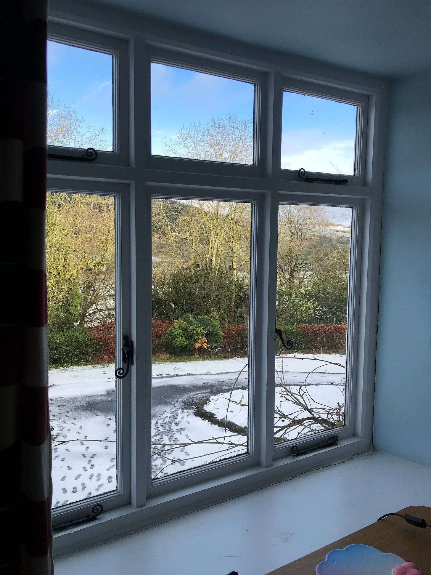 view at an angle through the window from a desk onto a snowy rural landscape, wooded hills in the distance.