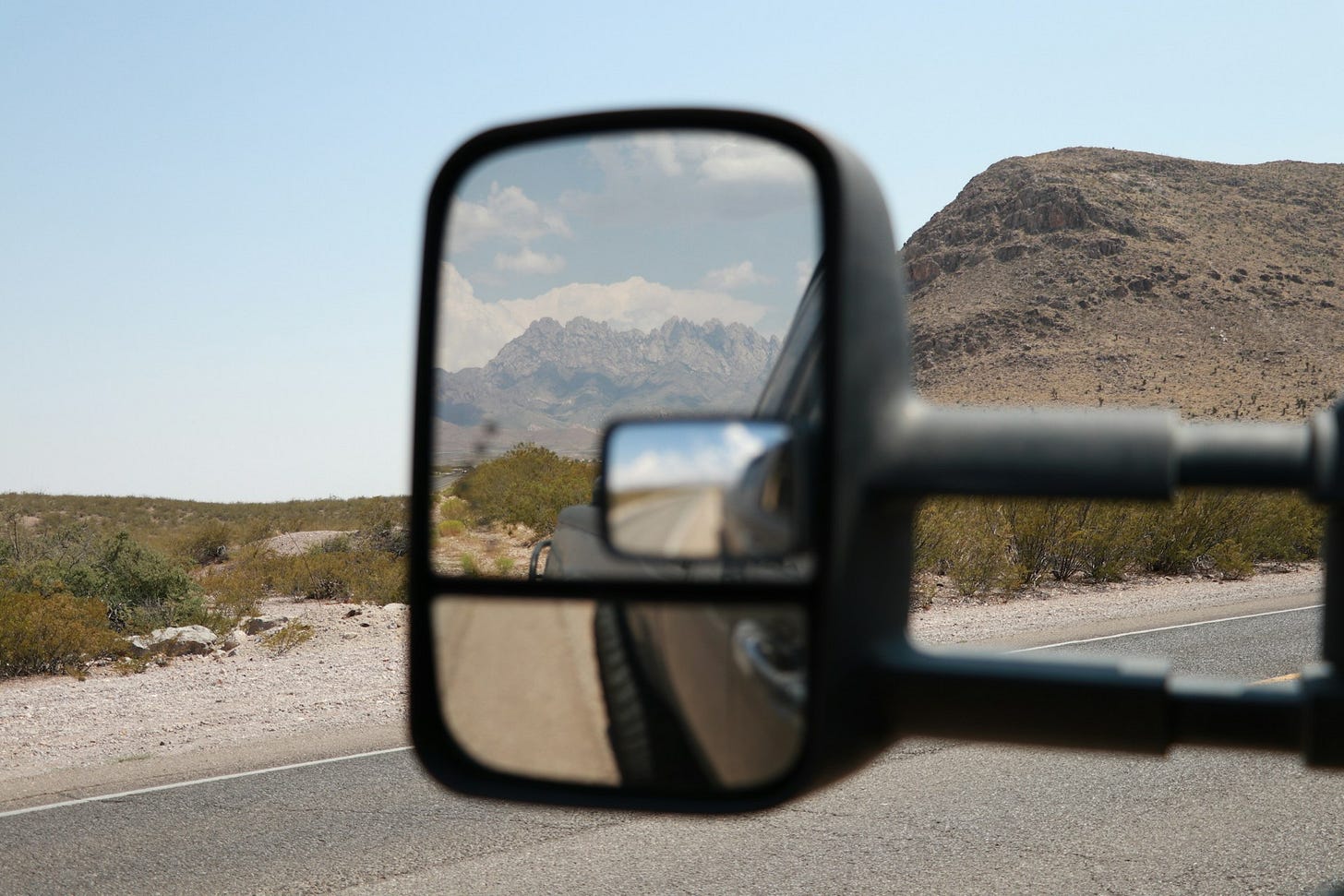 A truck's rear view mirror showing a mountain in the distance