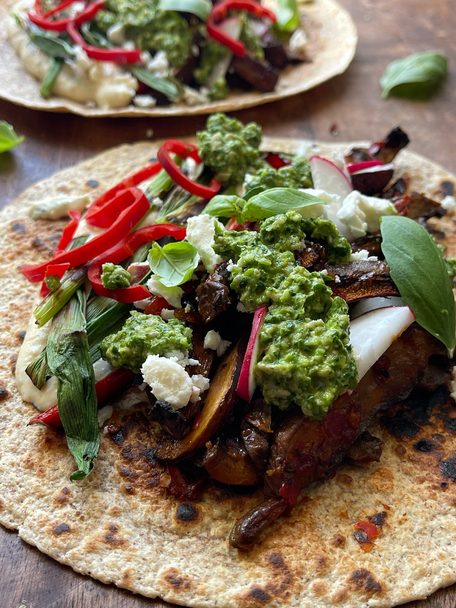 Close-up of a mushroom shawarma wrap with roasted portobello mushrooms, pistachio basil pesto, charred scallions, crumbled feta, sliced radishes, and red pepper in a toasted wheat wrap