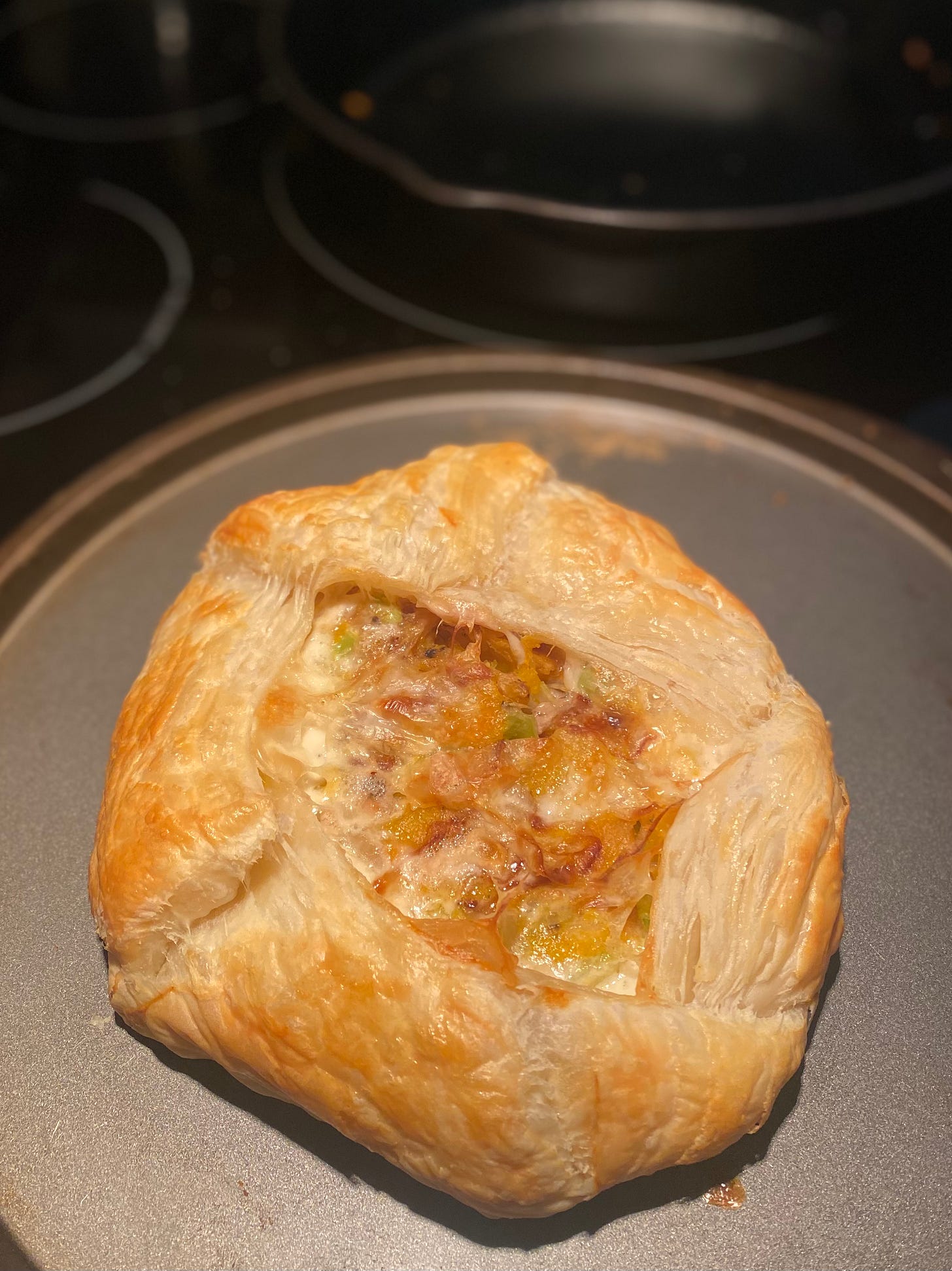 A puff pastry galette-style tart on a pizza pan. The centre is open and it's got orange squash, creamy melted cheese, and pieces of celery. There's a cast iron pan on the stove in the background.