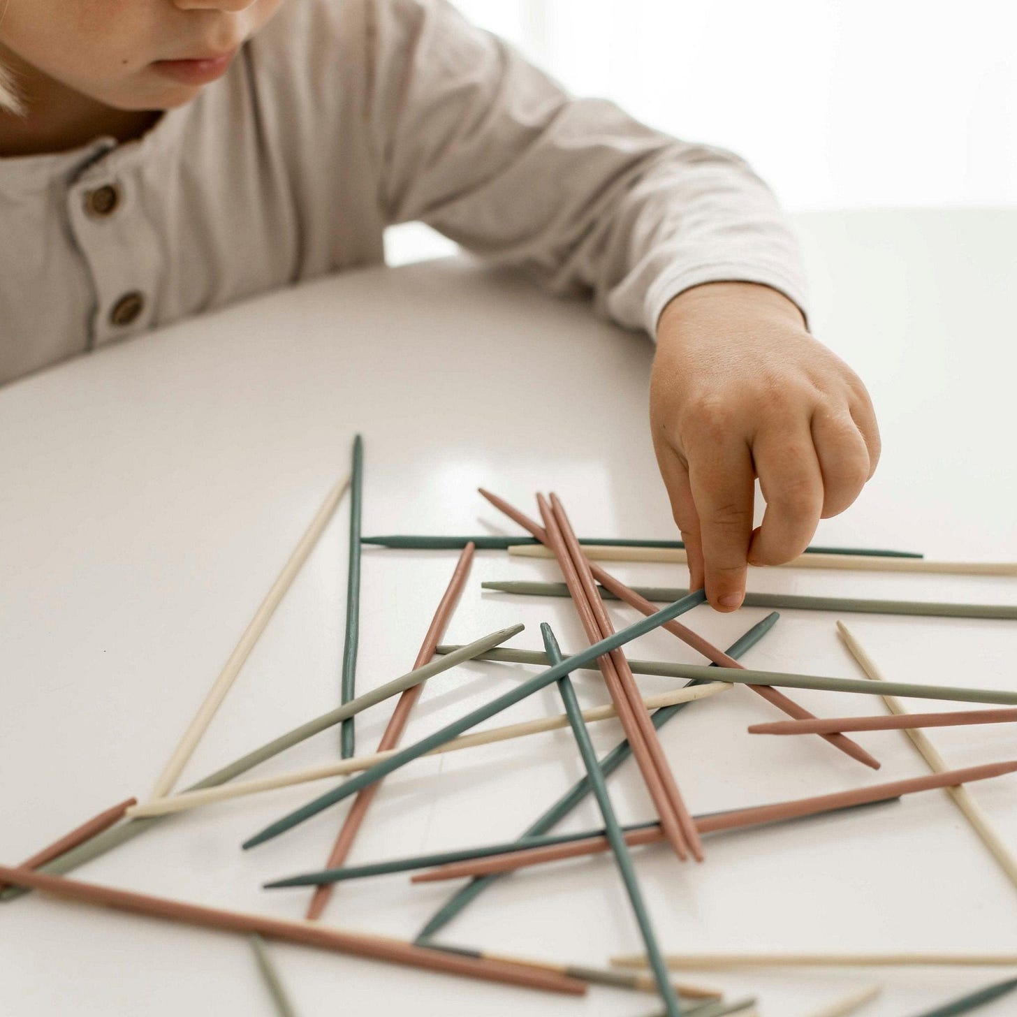A child's hand reaches out to remove a pickup stick from a pile