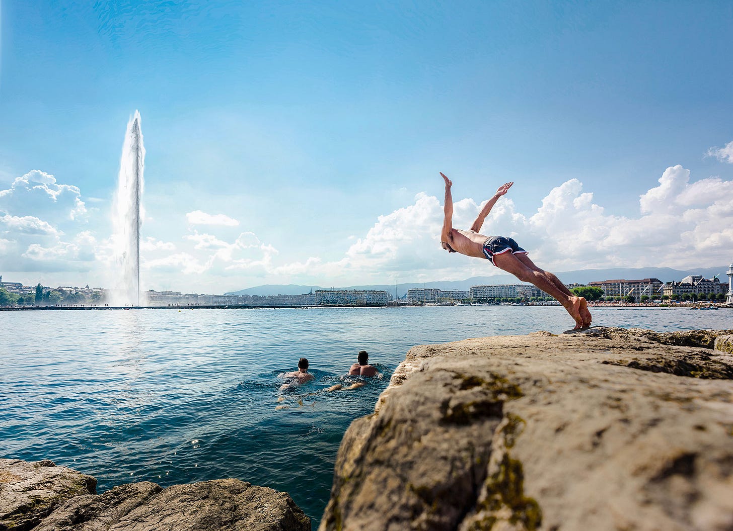 A swimmer diving into Lake Geneva with Jet D'Eau in the background.