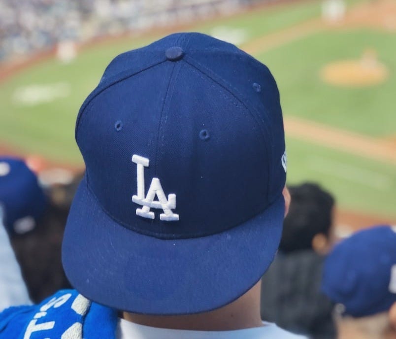 selective focus photography of person wearing LA Dodgers cap looking at field