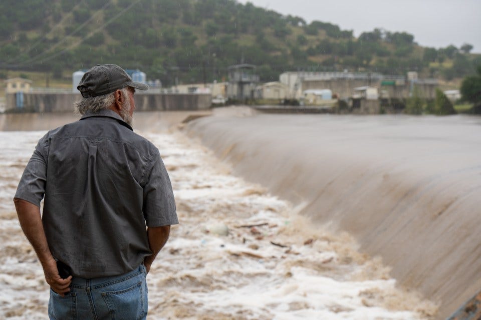 Man watching floodwaters rushing over a dam.