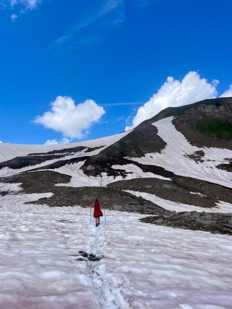 A woman hikes through a snow field on an alpine slope.