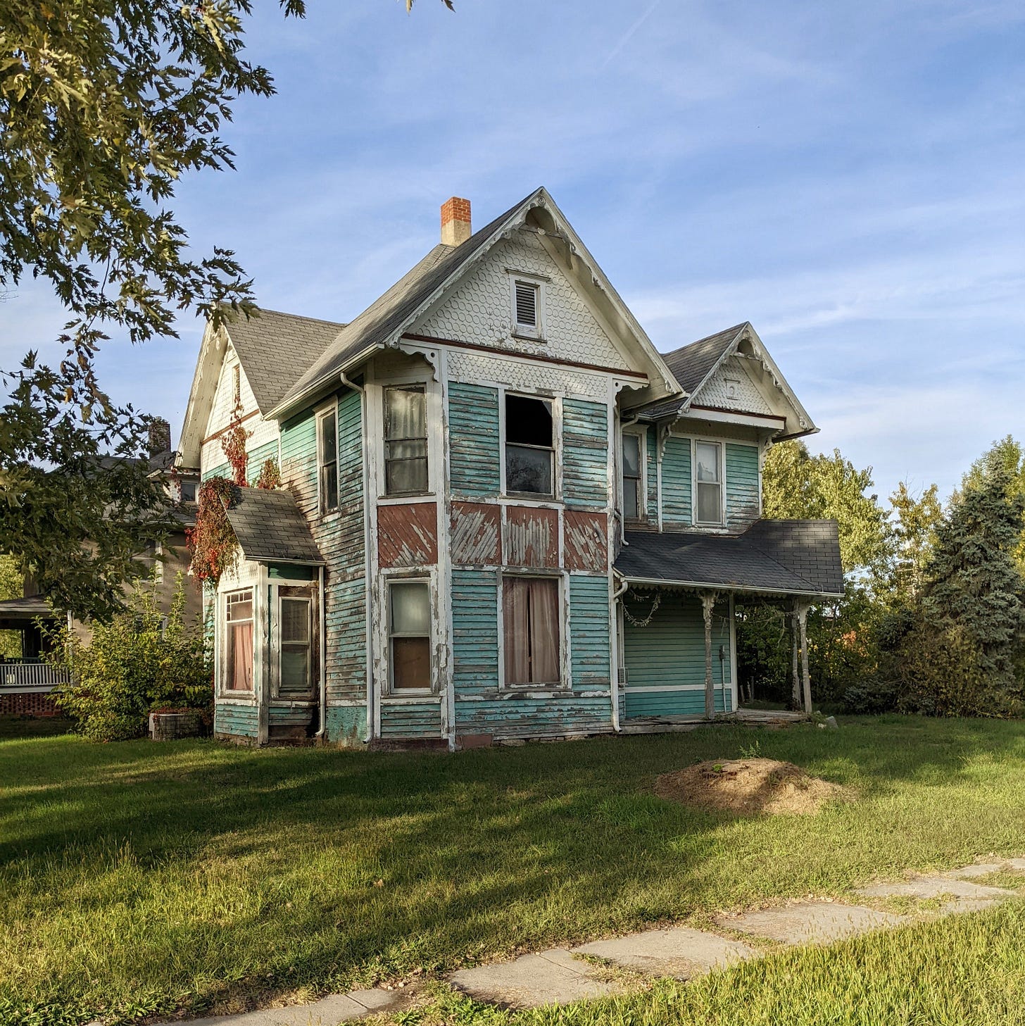 An abandoned Victorian house with peeling teal paint.