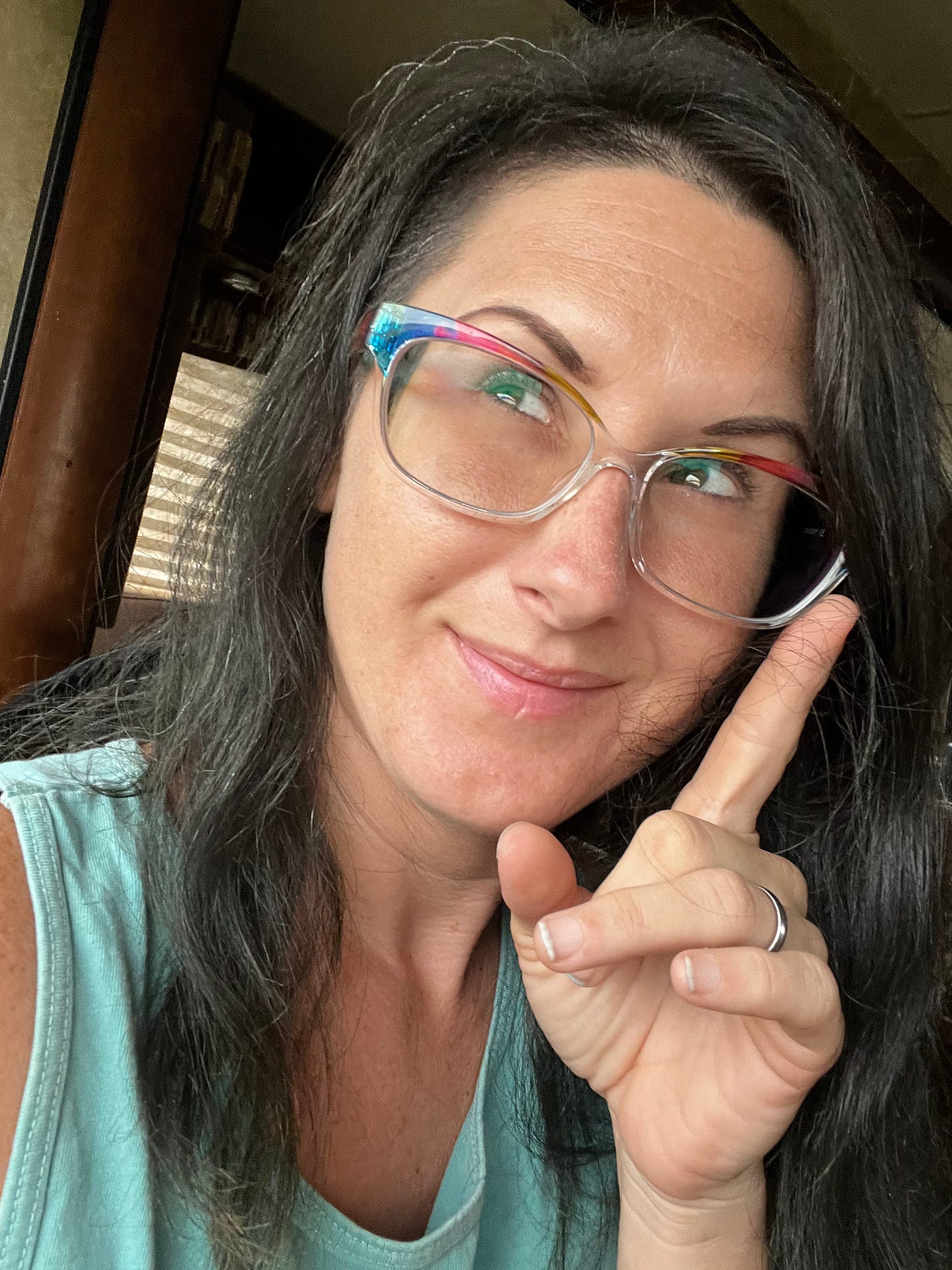 Lyric Rivera, with black and grey hair, a teal tank top, and rainbow glasses, sitting in an RV, smiling