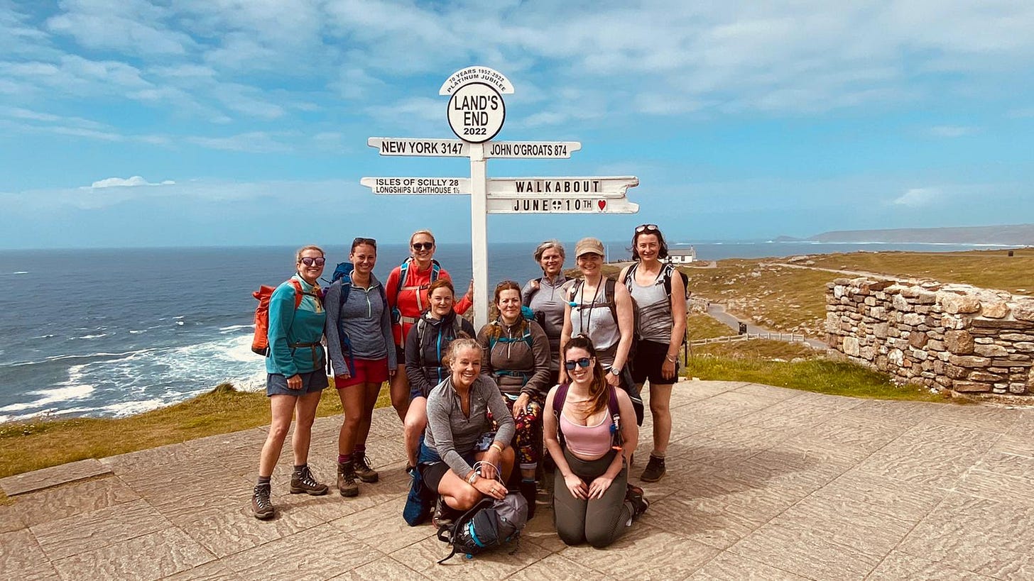 Colour photo of ten women standing in front of the sign post at Land's End, Cornwall UK