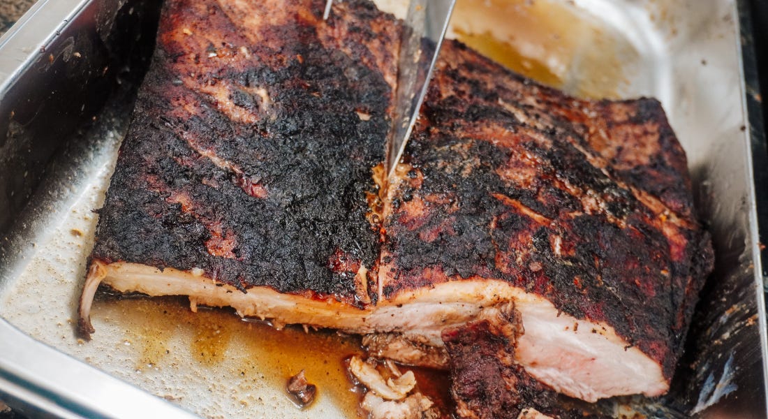 A pork belly loin being cut into, inside a silver tray