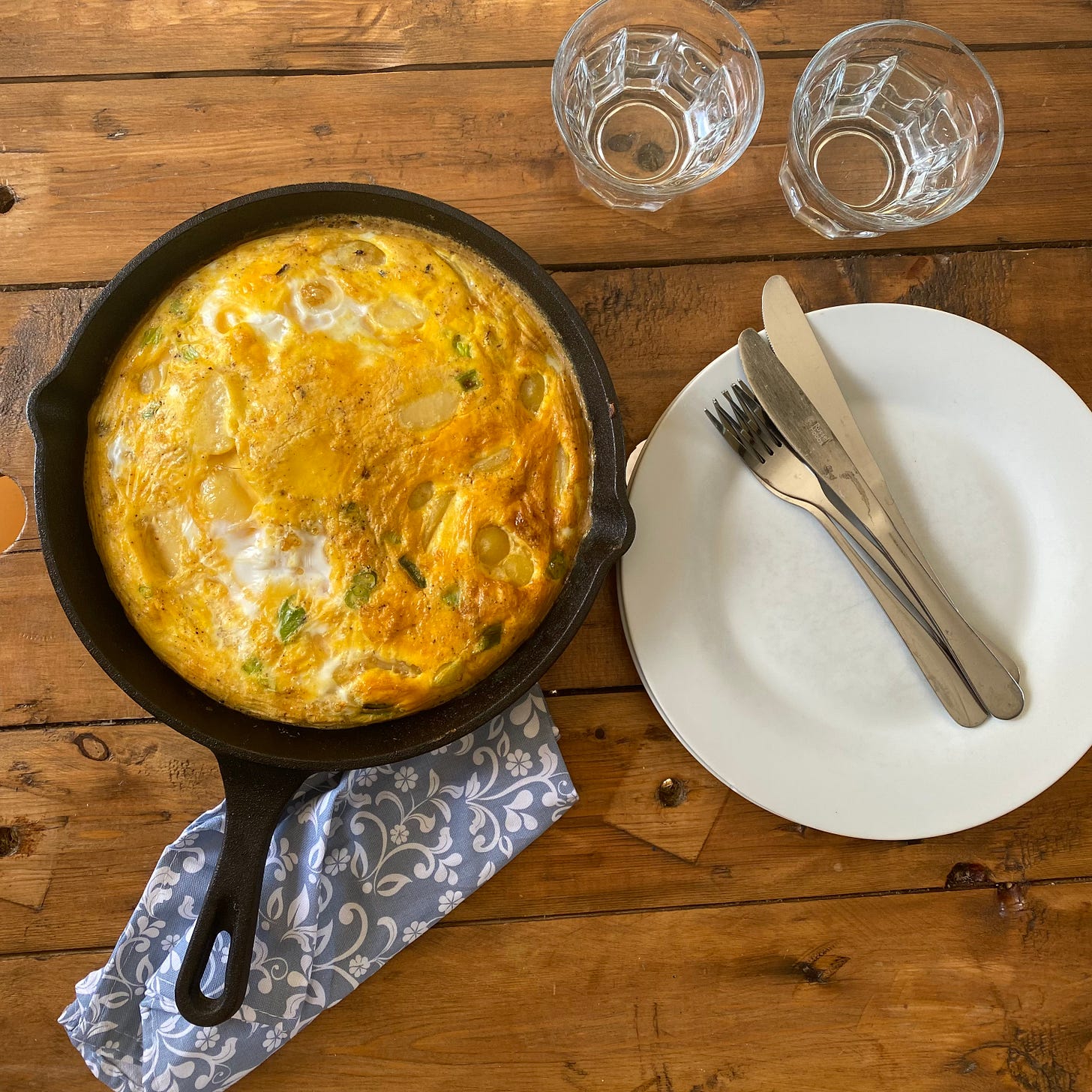 Table set with a pan of Spanish omelette, with plates, cutlery and water glasses to the side