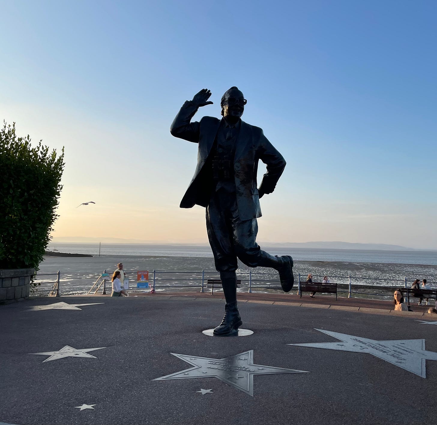 A statue of Eric Morecambe, in silhouette with a sunset behind him.