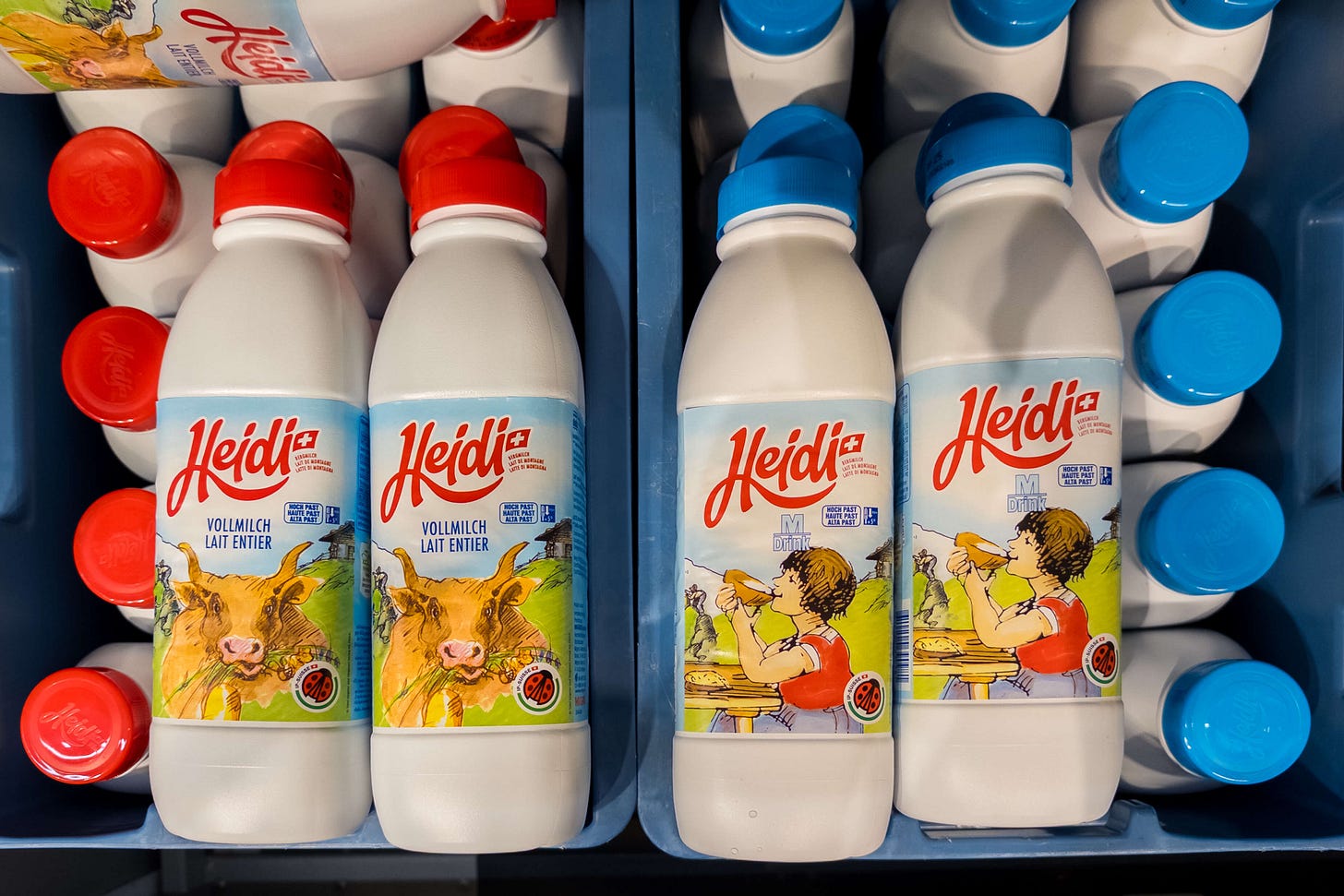 Mehrere Packungen «Heidi»-Milch mit rotem oder blauem Deckel in Kunststoffkisten. Mit rotem Deckel kVollmilch mit einer braunen Kuh, die Gras frisst, als Illustration. Mit blauem Deckel Milchdrink mit der Romanfigur Heidi, die an einem Holztisch sitzt und Brot isst. Beide Varianten tragen das IP-Suisse-Label mit dem Marienkäfer. Mehrere Packungen «Heidi»-Milch mit rotem oder blauem Deckel in Kunststoffkisten. Mit rotem Deckel kVollmilch mit einer braunen Kuh, die Gras frisst, als Illustration. Mit blauem Deckel Milchdrink mit der Romanfigur Heidi, die an einem Holztisch sitzt und Brot isst. Beide Varianten tragen das IP-Suisse-Label mit dem Marienkäfer.