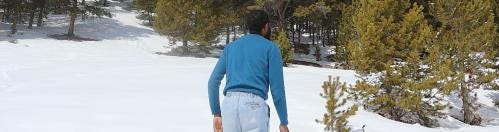 Jerome Ellis, wearing blue sweater and jeans, stands back to the viewer, in a clearing of snow with green trees in the background. Jerome Ellis, wearing blue sweater and jeans, stands back to the viewer, in a clearing of snow with green trees in the background.