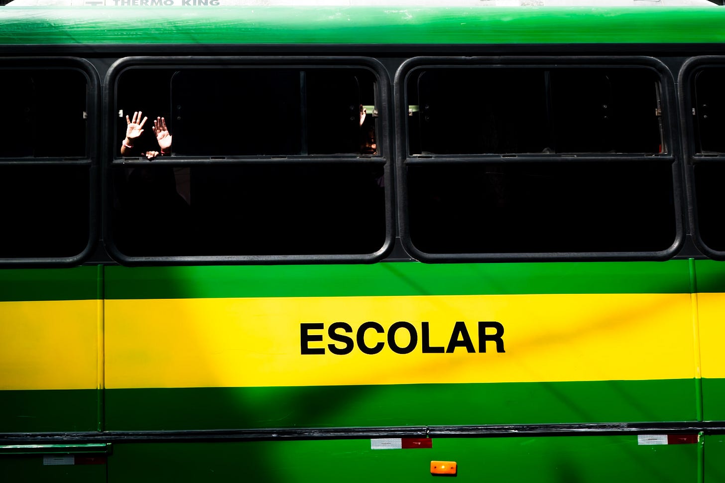 Hands of kids waving outside dark window of school bus