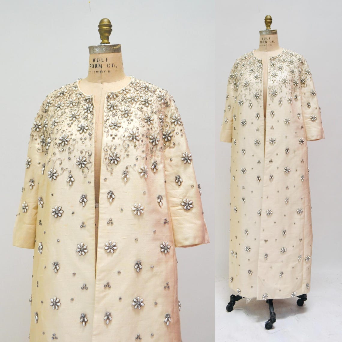 May include: A long, white, beaded coat with a floral design. The coat has a long, open front and three-quarter sleeves. The coat is displayed on a mannequin.