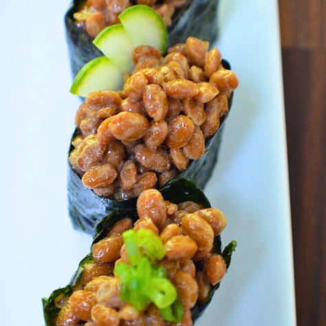 Three gunkan maki sushi pieces, each featuring a different plant-based topping: natto, spicy carrot tuna, and amaranth caviar. Each piece is wrapped in nori around a bed of rice, with the toppings held neatly on top.