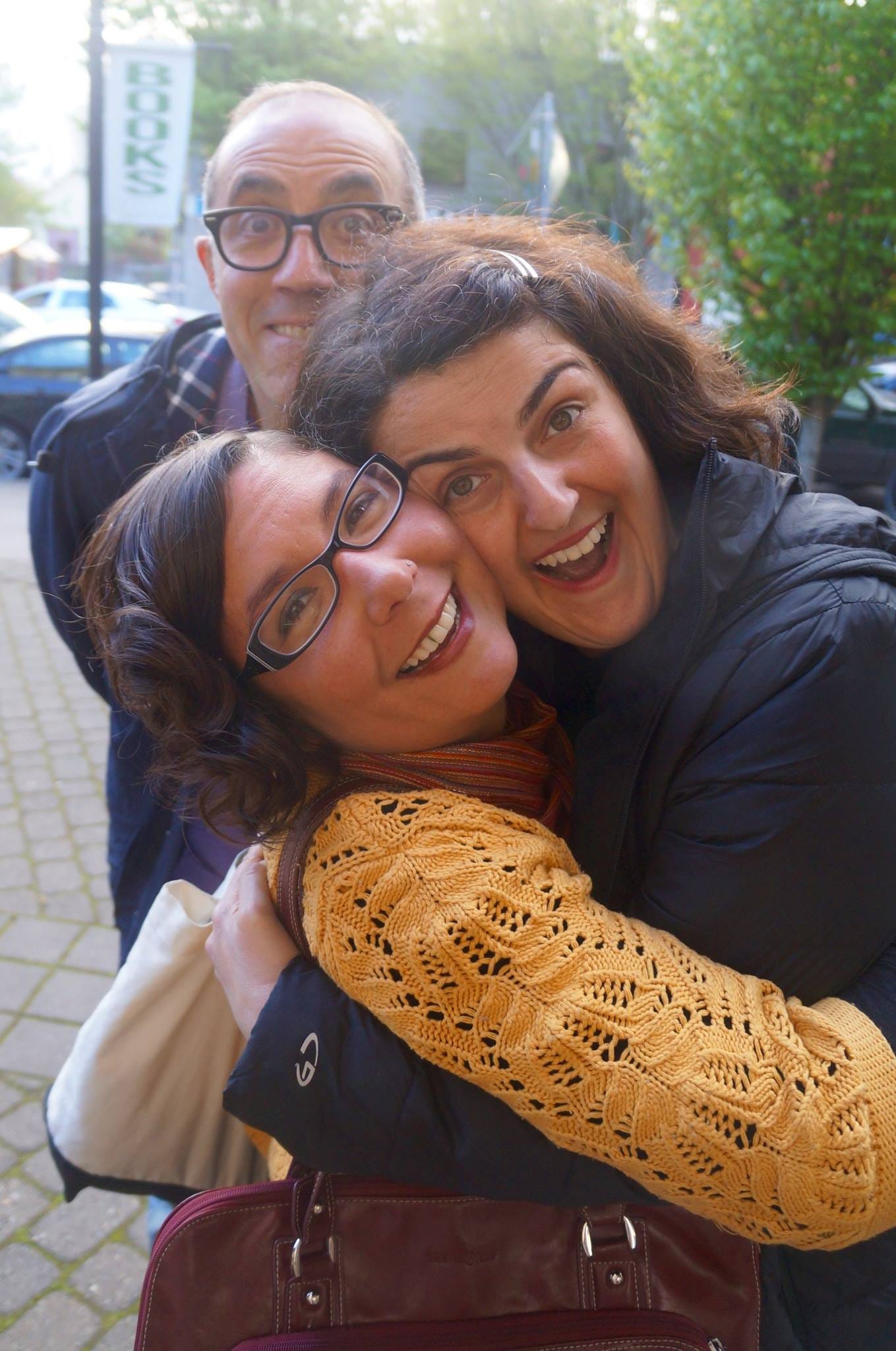 Three people clustered on a sidewalk, smiling big. 