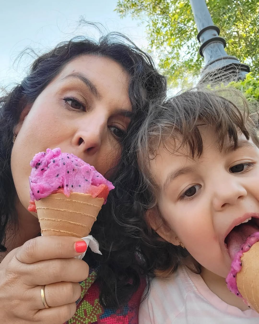 Denise and her young daughter smiling while eating pitaya and plum ice cream cones outdoors