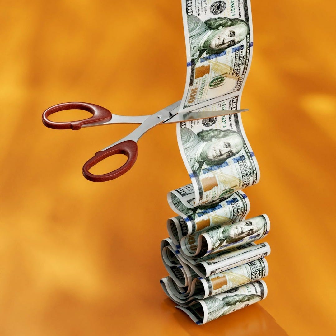 a stack of money sitting next to a pair of scissors a stack of money sitting next to a pair of scissors