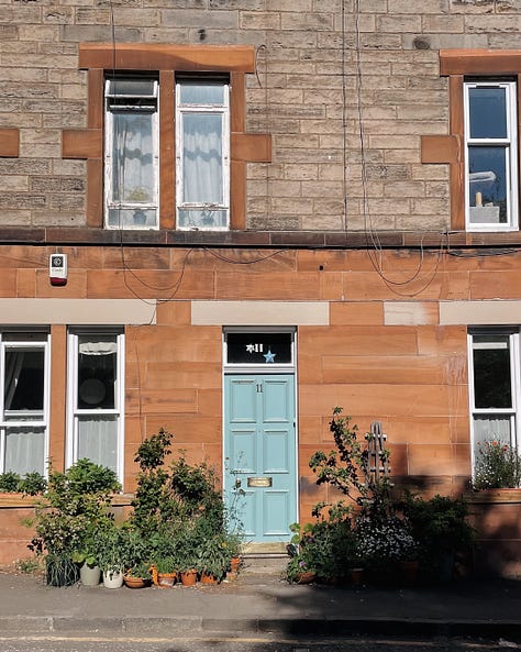 Gallery (3 images) - Image 1: Picnic setup with an open copy of Symposium, coffee in a reusable mug, and a half-eaten canelé. Image 2: Sunlit building front with greenery and a pale blue door. Image 3: My window with a cactus blooming with small pink flowers.