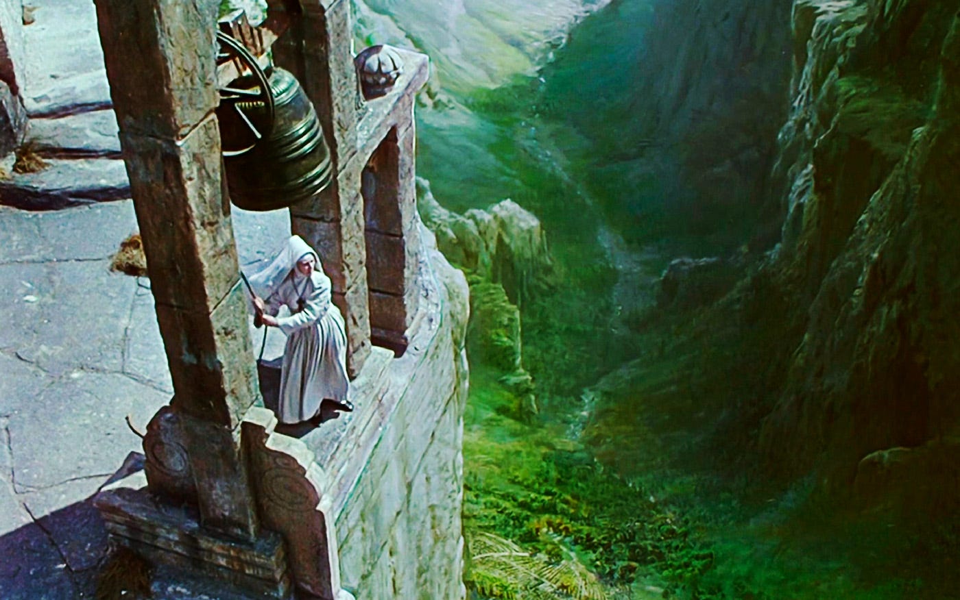 A nun in a white habit rings a massive bell atop a stone cliff, overlooking a lush green valley in Black Narcissus (1947). A nun in a white habit rings a massive bell atop a stone cliff, overlooking a lush green valley in Black Narcissus (1947).