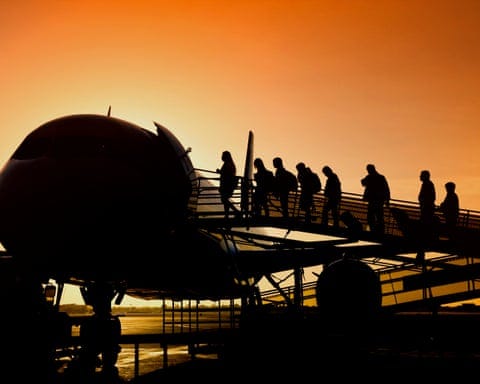 Silhouette of people boarding an airplane at sunset