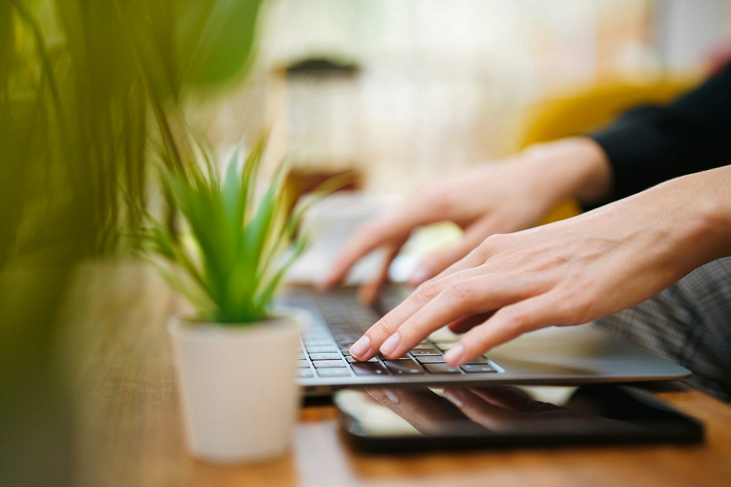 Close-up of hands typing on a laptop keyboard with a smartphone nearby, symbolizing digital tools for creating online polls. Photo by Jakub Zerdzicki on Unsplash