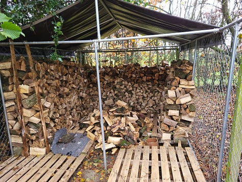 Former dog run ('Guantanamo') converted for log storage, with extended canvas roof protecting wood from rain. First picture shows Guantanamo from outside, with much reduced woodpile of split wood awaiting storage. Also, some remaining ash tree rings yet to be split. Big, beautiful, blue November sky, with morning frost on the grass, with trees and bushes mid-picture. Second photo shows 'Guantanamo' half filled with logs, the extension to the roof yet to be fitted. Third picture shows completed 'Guantanamo' filled with split logs and the extension of the canvas roof in place.