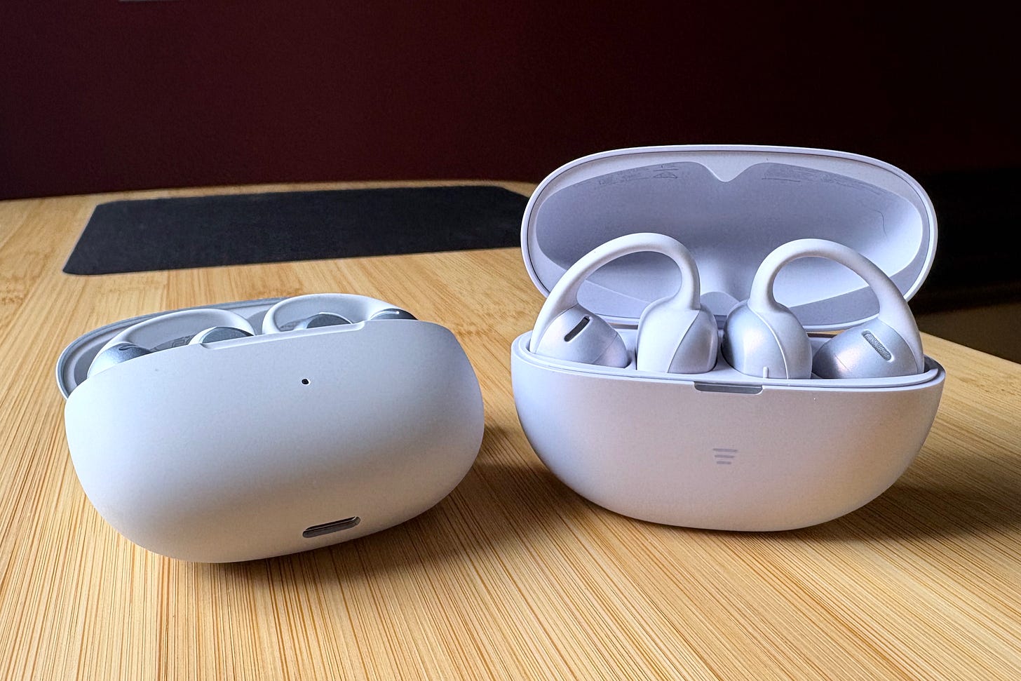 Shokz OpenDots 2 and OpenDots Air, sitting side by side, with charging case lids open. Shokz OpenDots 2 and OpenDots Air, sitting side by side, with charging case lids open.