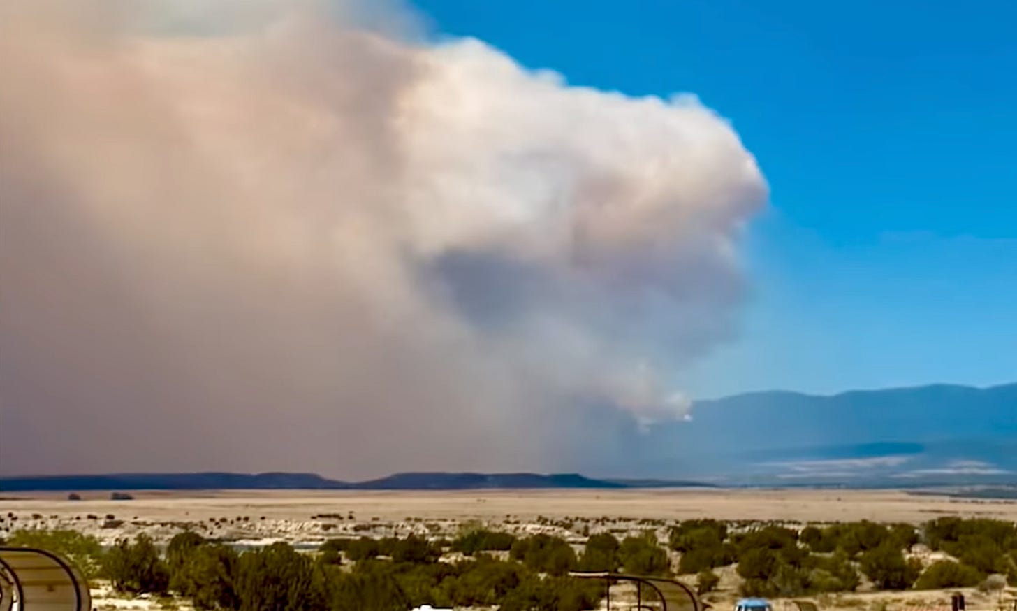 Smoke crossing sky dwarfs a mountain range.