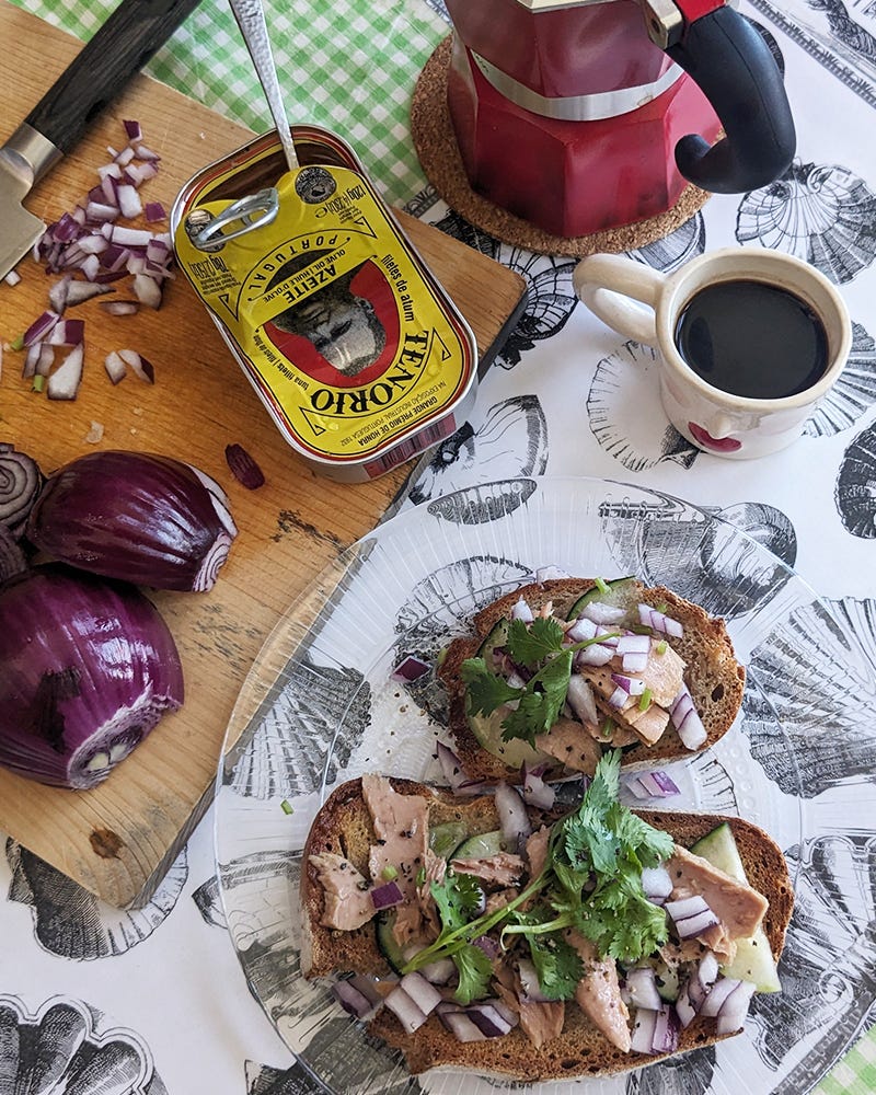 Photo of a lunch of toast with tuna filet, cucumber, cilantro, onion, and pepper. On the table are chopped onions and an open can of tuna on a cuttingboard, a red moka pot, and coffee in a small white espresso cup. Photo of a lunch of toast with tuna filet, cucumber, cilantro, onion, and pepper. On the table are chopped onions and an open can of tuna on a cuttingboard, a red moka pot, and coffee in a small white espresso cup.