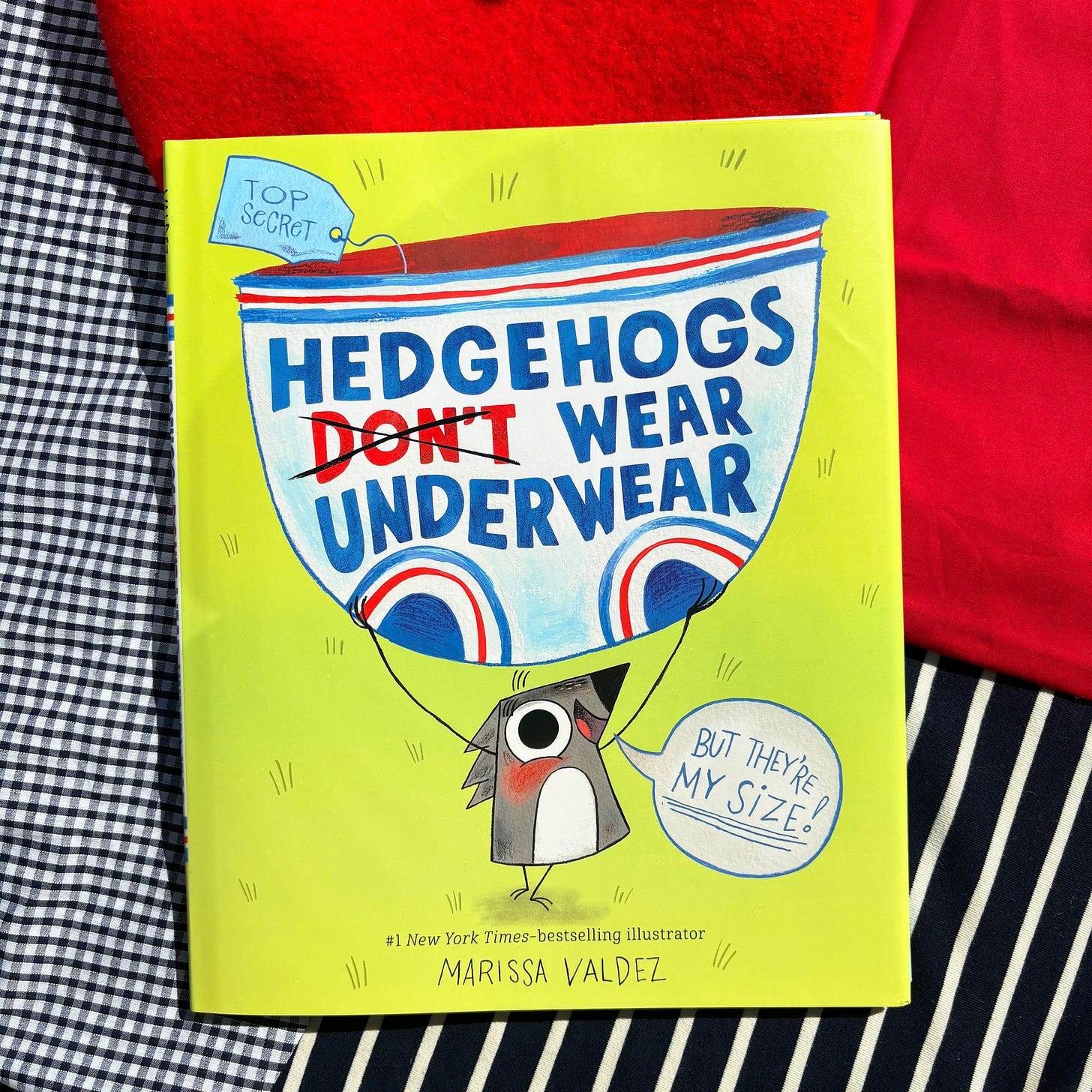 The picture book, Hedgehogs Don't Wear Underwear, on several french-looking fabrics. A red beret sits nearby.