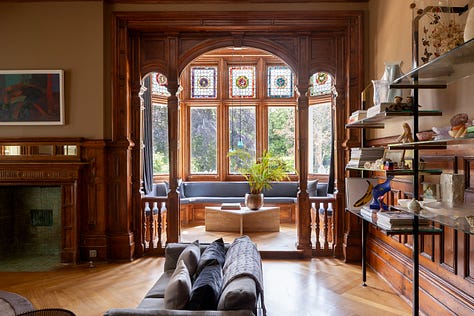 A wooden bay window with blue seat, a soft pink dining room with antique table, a small living room with a sofa and ottoman