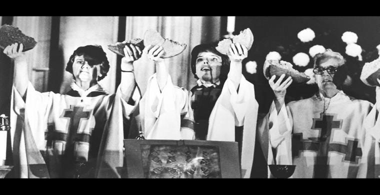 Three women in priestly garments holding up bread to consecrate it