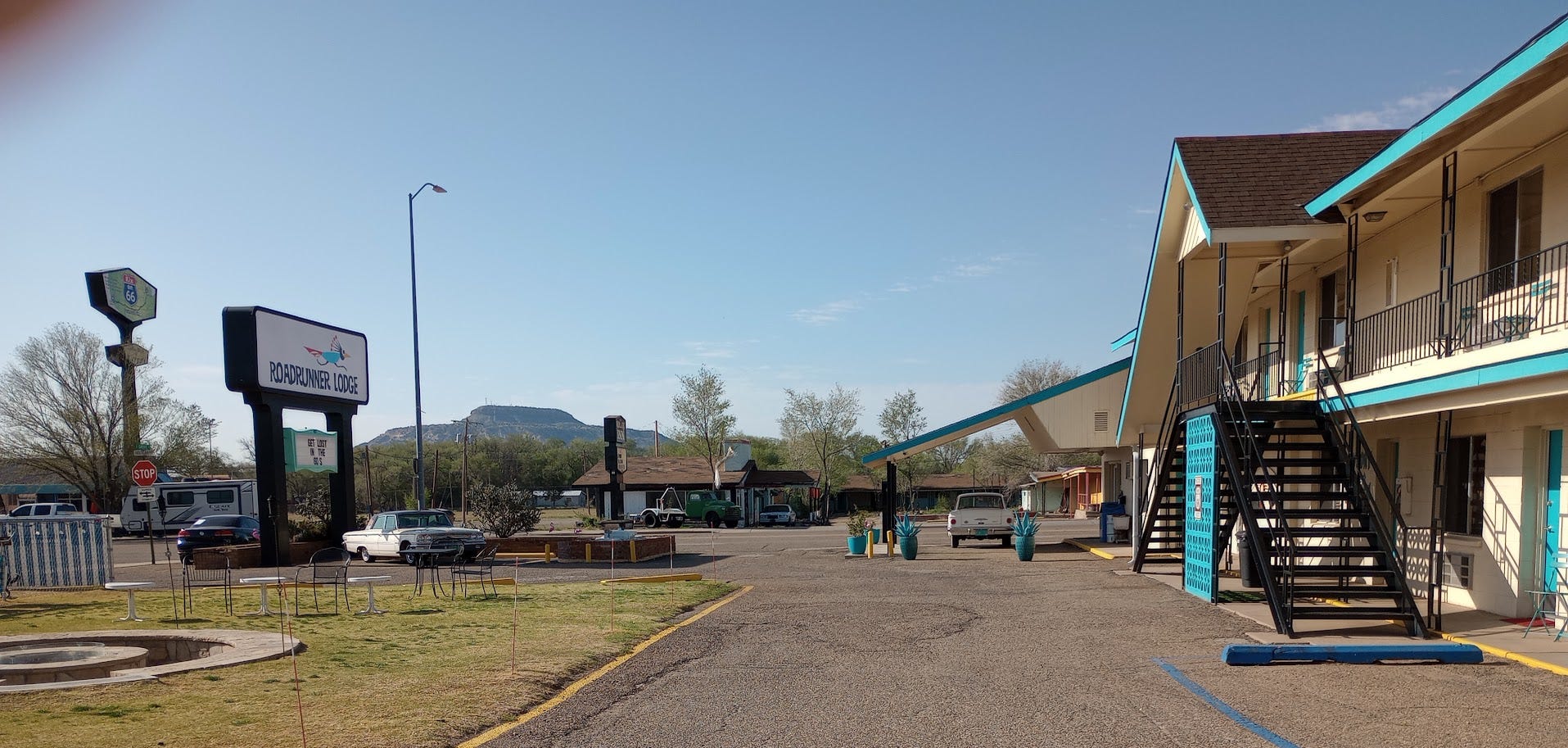 Two=story motel with 1960s cars in front of Roadrunner Lodge sign and motel office