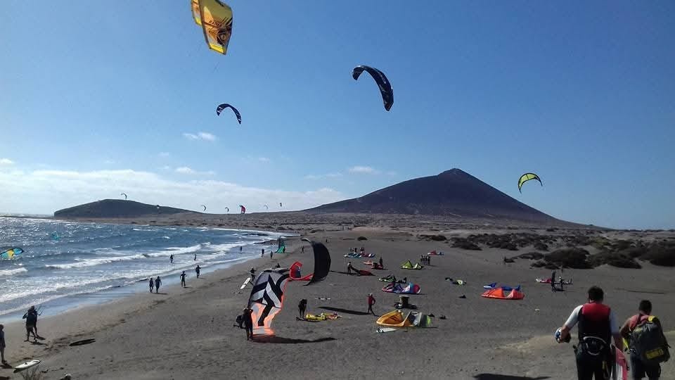 Red mountain with the surf beach in front. Many kite surfers setting up their kites.